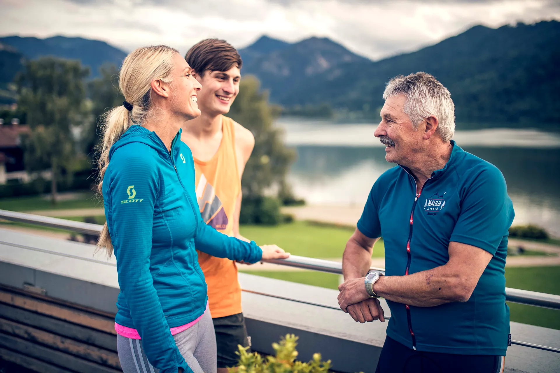 Drei Sportler im Gespräch auf einer Terrasse mit Blick auf den Schliersee