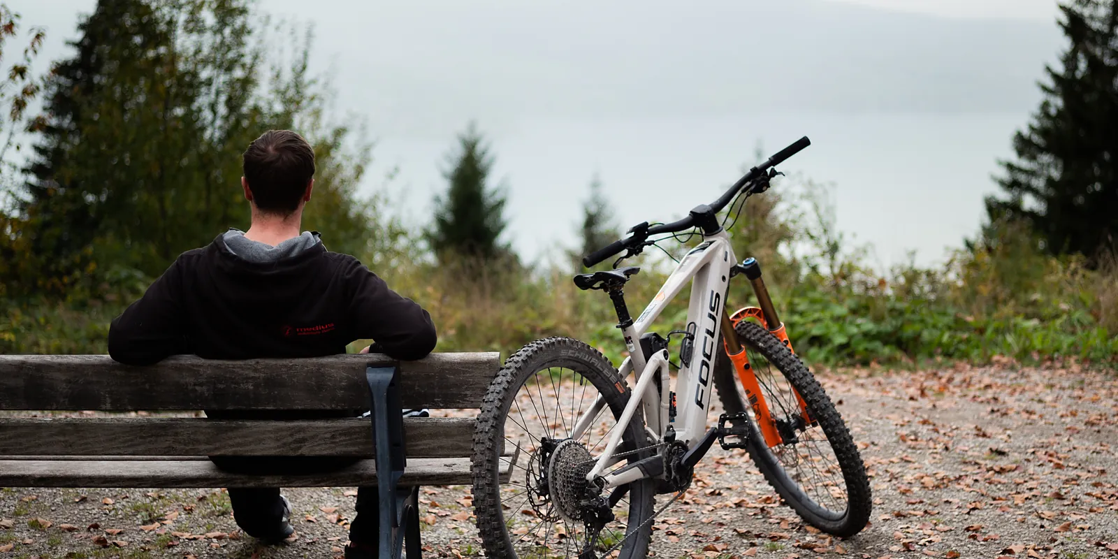 Radfahrer mit E-Bike auf einer Bank mit Blick auf den Tegernsee