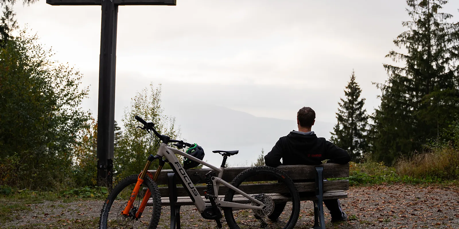Radfahrer rastet am Gipfelkreuz über dem Tegernseer Tal